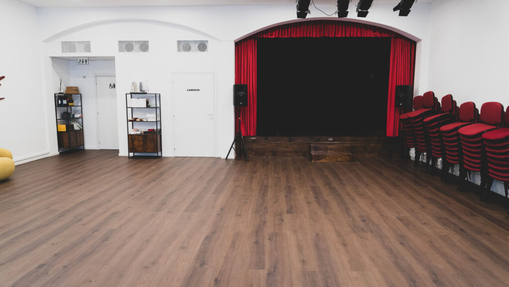 La sala del Teatro degli Audaci Off con il palco, il sipario rosso e le sedie di velluto rosso